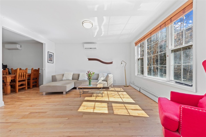 Living room featuring wood finished floors, an AC wall unit, and baseboard heating
