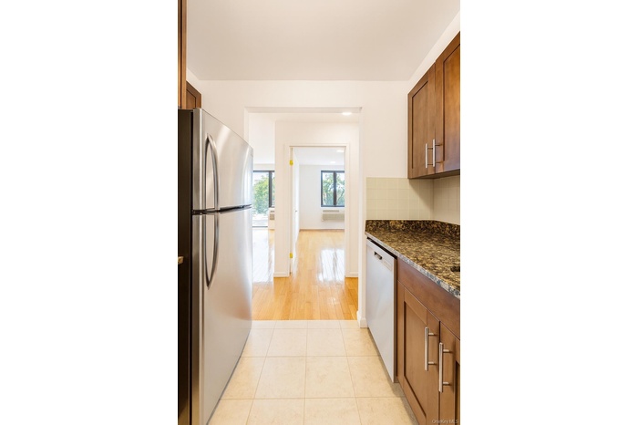 Kitchen with brown cabinetry, freestanding refrigerator, dark stone countertops, and dishwasher