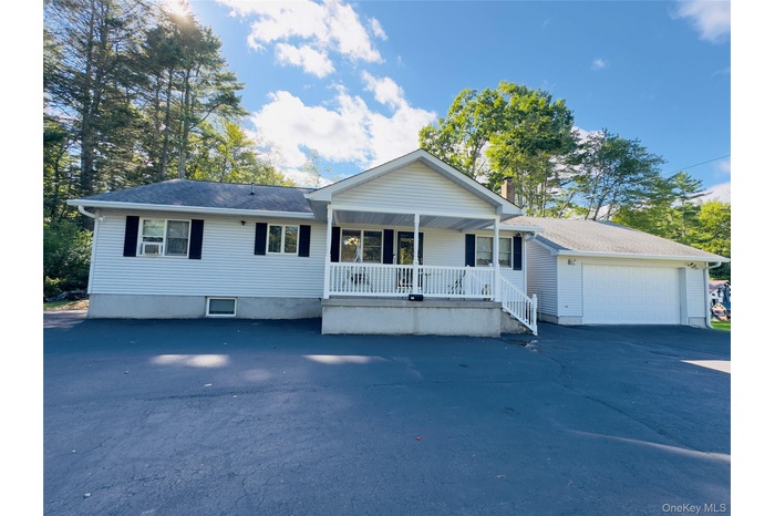 Single story home featuring a porch, paved driveway, detached garage