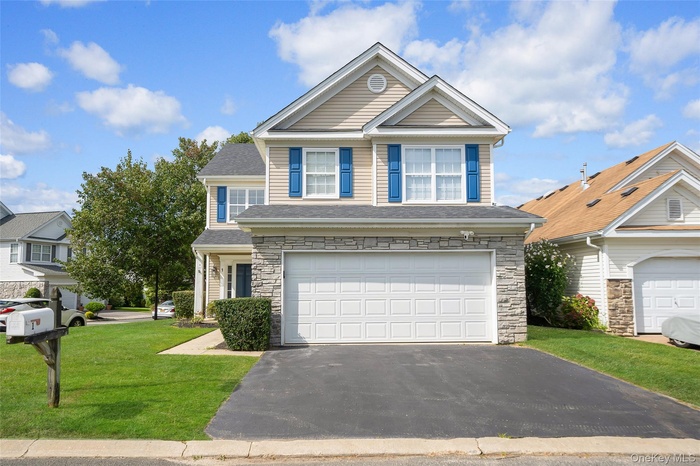 Traditional home featuring stone siding, driveway, a front yard, a garage, and a shingled roof