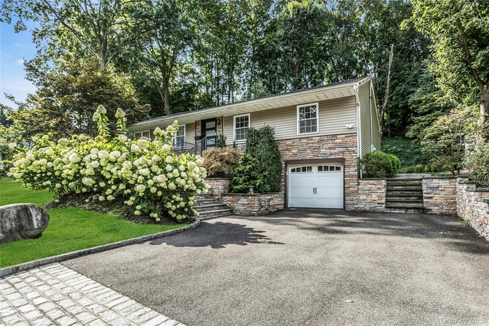View of front of property featuring stone siding, driveway, and a garage