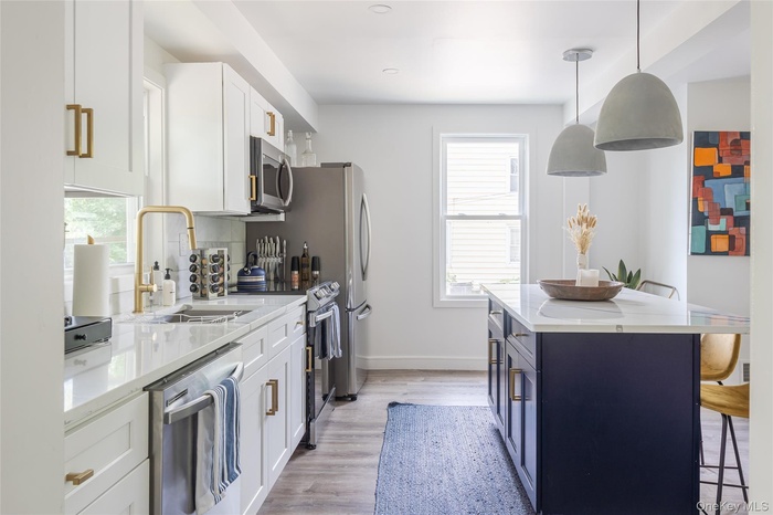 Kitchen with white cabinets, light stone counters, a breakfast bar, hanging light fixtures, and light wood finished floors