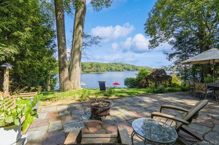 View of patio featuring a fire pit, a water view, outdoor dining area, and a forest view