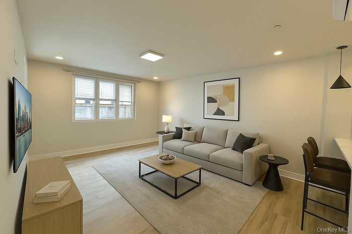 Living area with light wood-type flooring, recessed lighting, and a wall mounted air conditioner