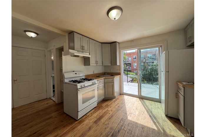 Kitchen with gray cabinetry, white appliances, light wood finished floors, and under cabinet range hood