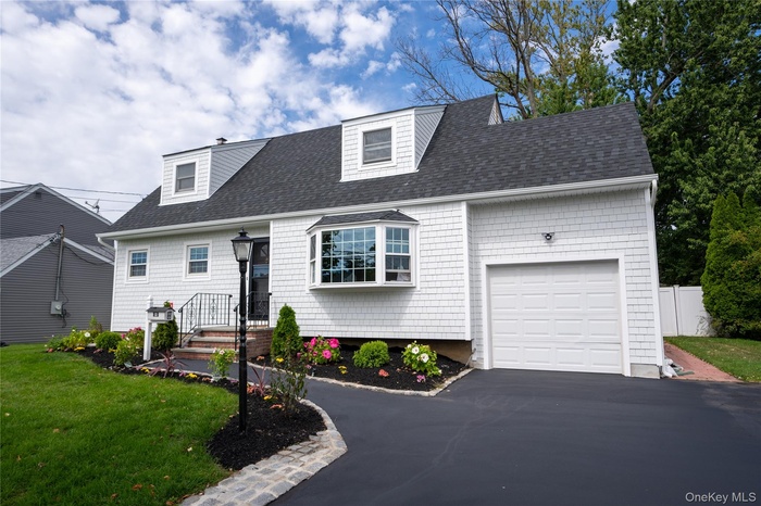 Cape cod-style house with a shingled roof, a garage, and asphalt driveway