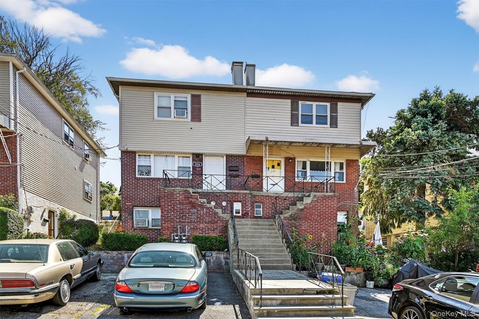 View of front of property featuring stairway, brick siding, and uncovered parking