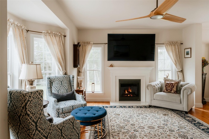 Living area featuring a glass covered fireplace, wood finished floors, and ceiling fan