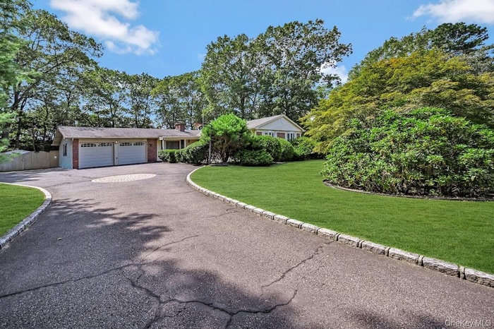 Ranch-style house with a front lawn, asphalt driveway, brick siding, a chimney, and an attached garage