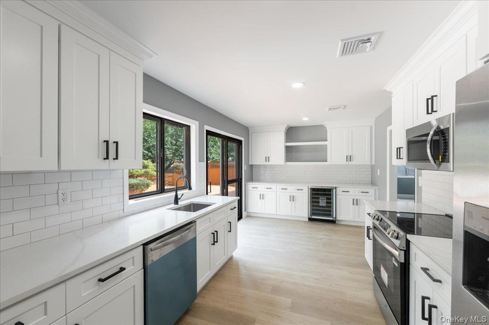 Kitchen featuring white cabinetry, open shelves, appliances with stainless steel finishes, light stone counters, and recessed lighting
