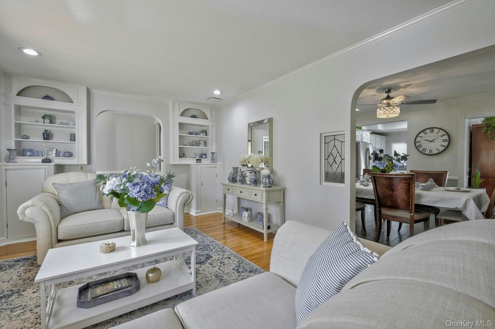 Living room with arched walkways, wood finished floors, crown molding, built in shelves, and recessed lighting