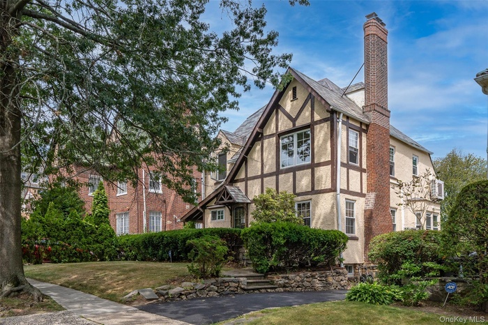 Tudor-style house featuring stucco siding, a front lawn, and a chimney