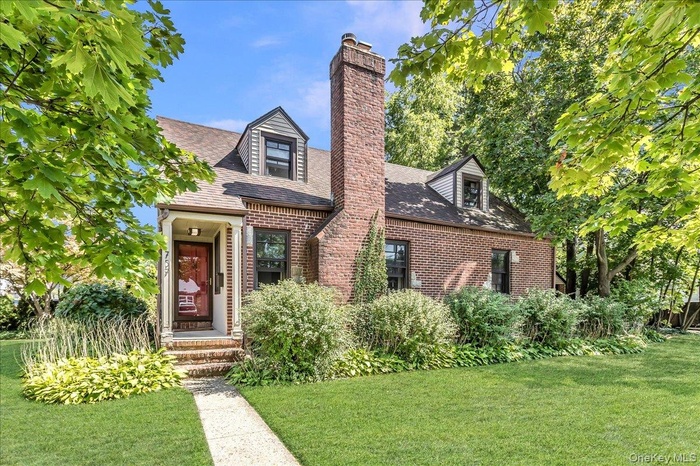 View of front facade with brick siding, a front lawn, and a chimney