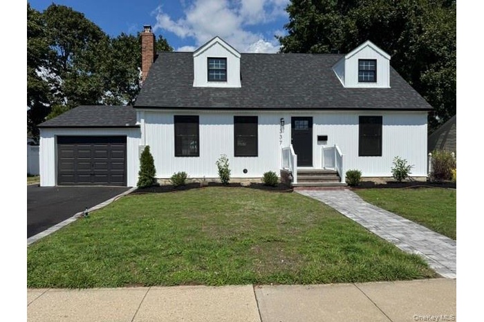 View of front facade featuring a front yard, asphalt driveway, a shingled roof, and a chimney