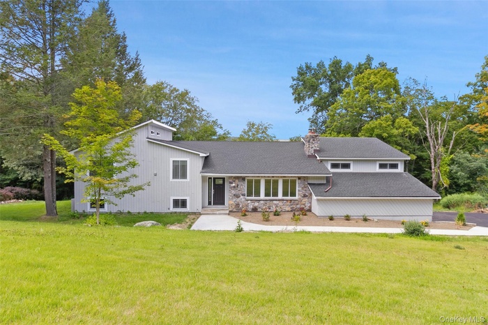 Back of property featuring stone siding, a lawn, a chimney, and a shingled roof