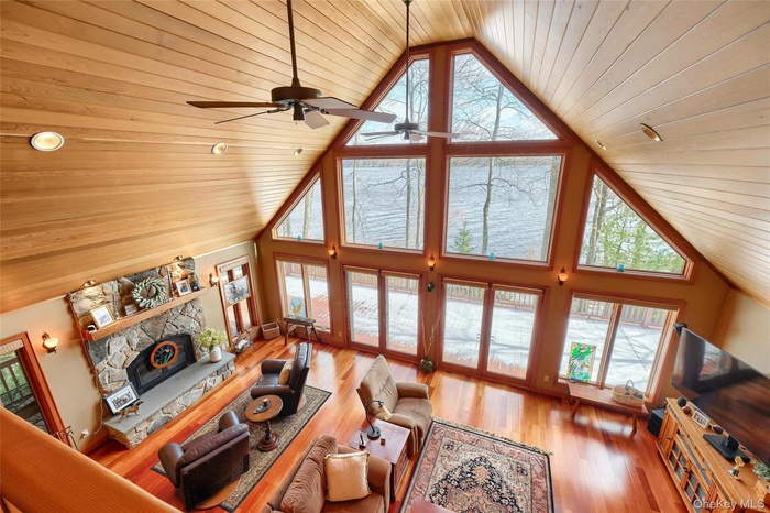 Living area with wood ceiling, plenty of natural light, high vaulted ceiling, a ceiling fan, and a fireplace