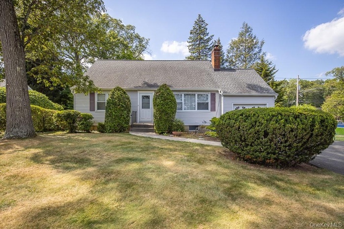 View of front facade featuring a chimney, a front lawn, an attached garage, and a shingled roof