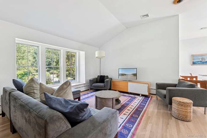 Living area with vaulted ceiling, wood finished floors, and baseboard heating
