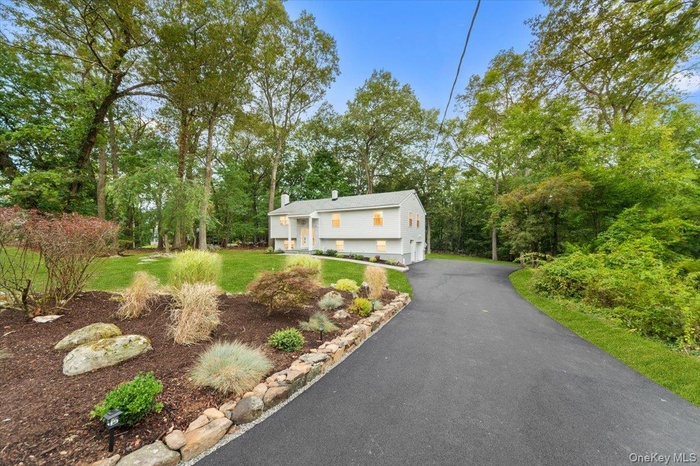 Bi-level home featuring driveway, a front lawn, and view of scattered trees