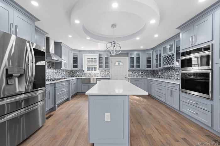Kitchen featuring gray cabinets, stainless steel appliances, a raised ceiling, recessed lighting, and a kitchen island