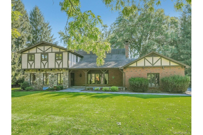 Tudor house with covered porch, a chimney, a front lawn, and brick siding