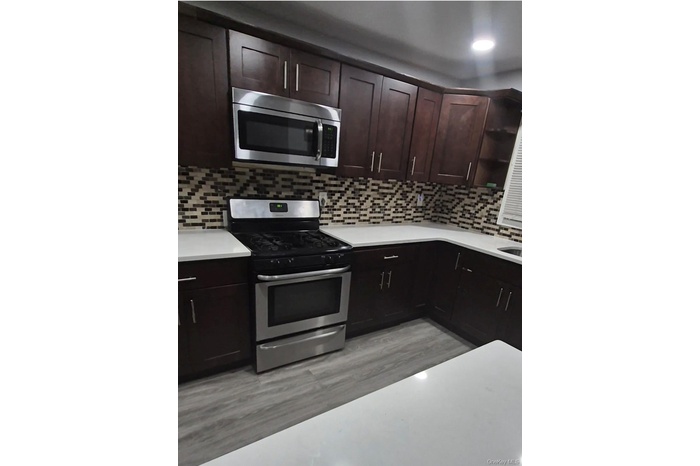 Kitchen with appliances with stainless steel finishes, dark brown cabinetry, light wood finished floors, tasteful backsplash, and open shelves