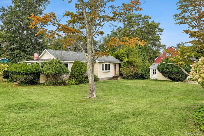 View of front of property with a front yard, view of wooded area, a storage unit, and roof with shingles