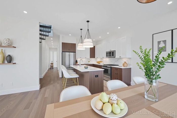 Kitchen with decorative light fixtures, a kitchen island with sink, backsplash, appliances with stainless steel finishes, and white cabinetry