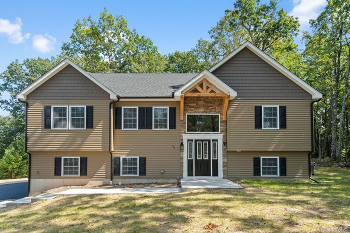 View of front of home with a front lawn, stone siding, and a shingled roof