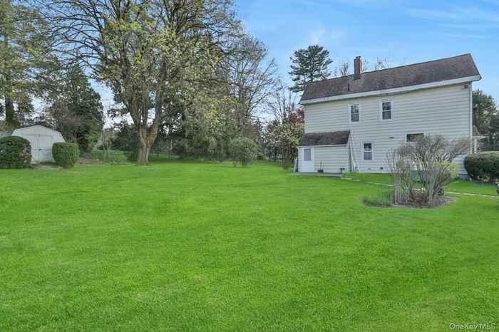 Back of property with a chimney, a lawn, a shingled roof, and a shed