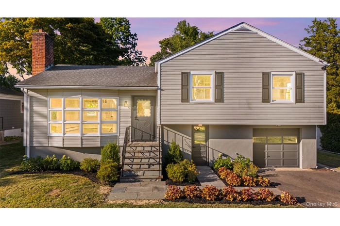 Tri-level home featuring a garage, a shingled roof, a chimney, driveway, and stucco siding