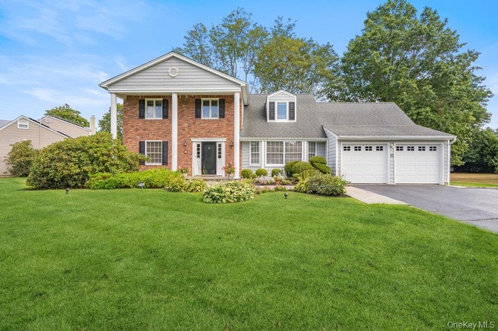 Greek revival house with a front lawn, a garage, asphalt driveway, a shingled roof, and brick siding