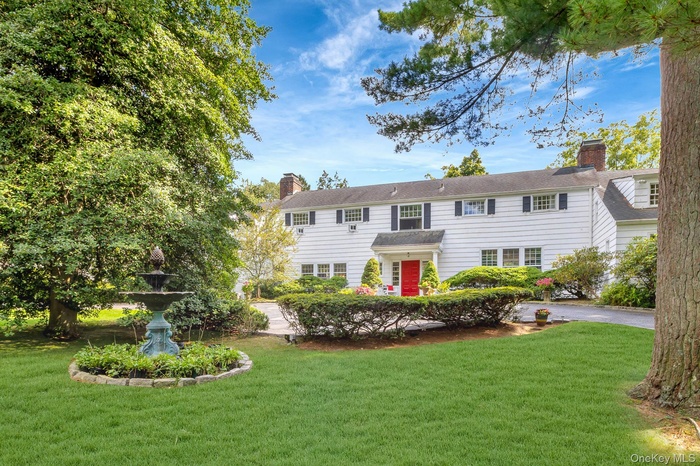 Colonial home featuring a front lawn and a fountain