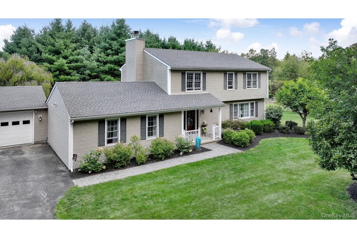 View of front facade with a front lawn, roof with shingles, a garage, and a chimney