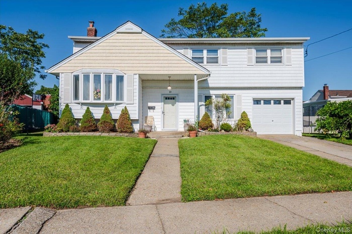 View of front facade featuring a garage, a chimney, and driveway