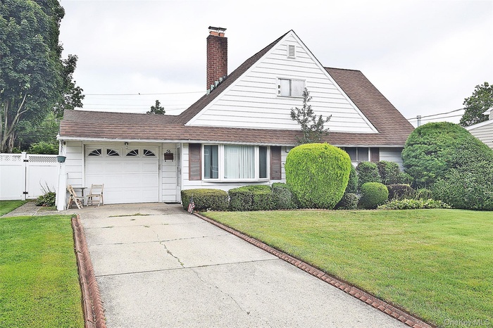 View of front of house featuring a shingled roof, an attached garage, concrete driveway, and a chimney