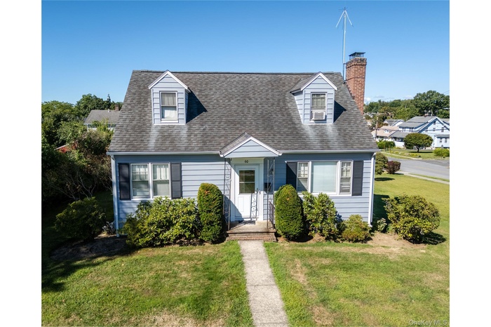 Cape cod-style house with a chimney, a front lawn, and a shingled roof