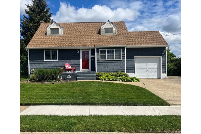 Cape cod home with a garage, a front lawn, a shingled roof, concrete driveway, and a chimney