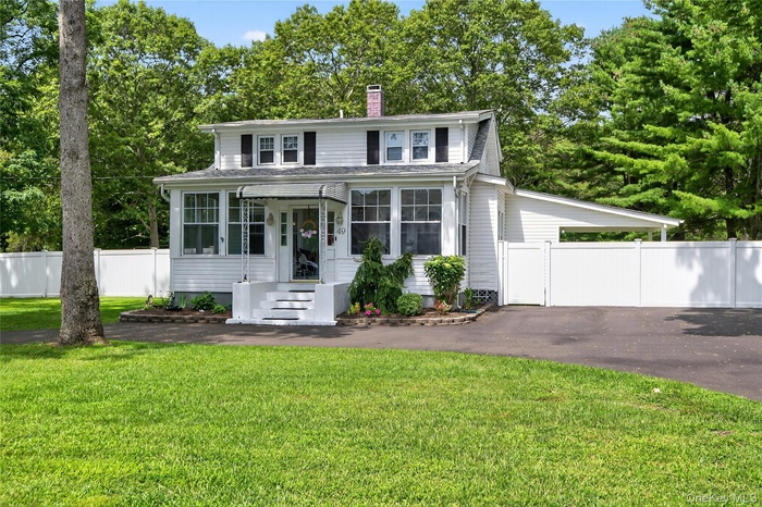 View of front of property with asphalt driveway, a chimney, view of scattered trees, and a carport