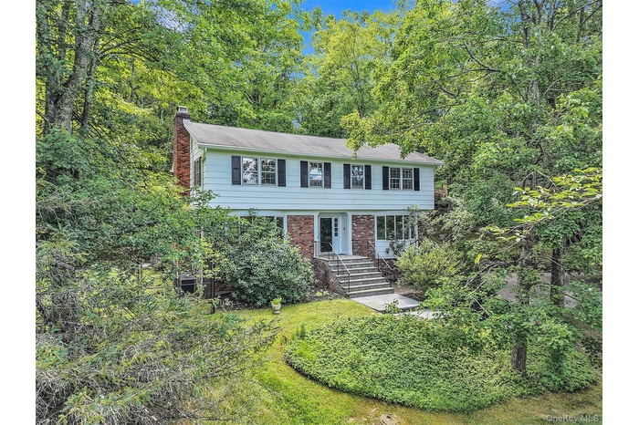Colonial home featuring a chimney, brick siding, and a view of trees