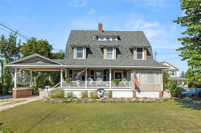 View of front of house with covered porch, roof with shingles, a front lawn, and a chimney