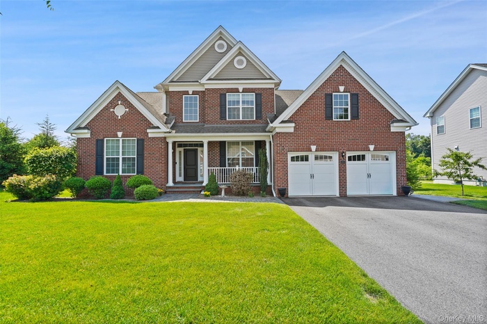 View of front of home featuring covered porch, brick siding, asphalt driveway, and a front yard
