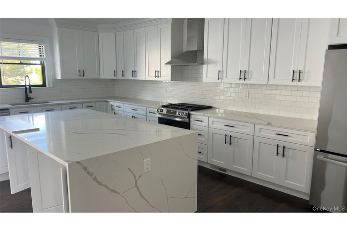 Kitchen with appliances with stainless steel finishes, a kitchen island, white cabinets, wall chimney range hood, and light stone countertops