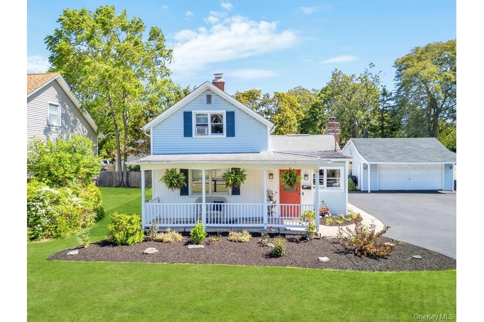 View of front of property featuring a chimney, covered porch, a garage, a front yard, and asphalt driveway