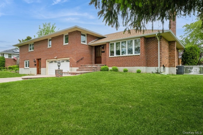 Tri-level home featuring a garage, concrete driveway, a chimney, brick siding, and central air condition unit
