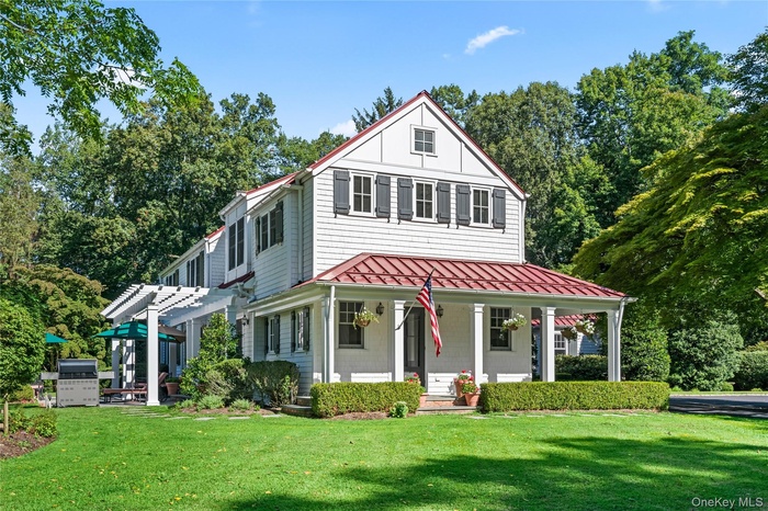 View of front facade with a standing seam roof, a front yard, a metal roof, a porch, and view of wooded area