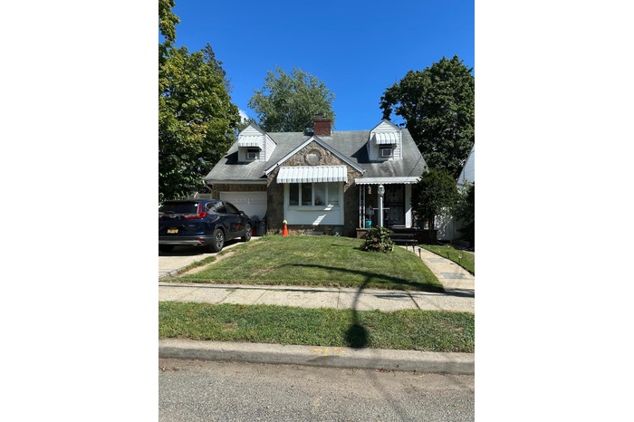 View of front of property with a garage, a front lawn, a chimney, driveway, and a shingled roof