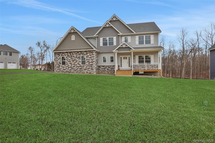 Craftsman-style house with stone siding, a porch, a front yard, and a shingled roof