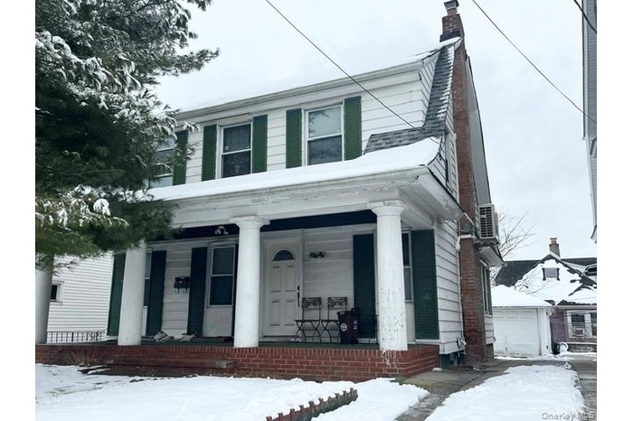 View of front of home featuring covered porch, a chimney, and a garage