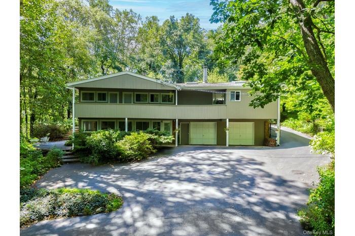 View of front of property with asphalt driveway, a garage, a balcony, and view of scattered trees